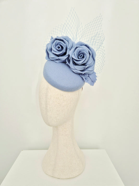 Dusty blue fascinator with flowers on a mannequin head against a white background side view