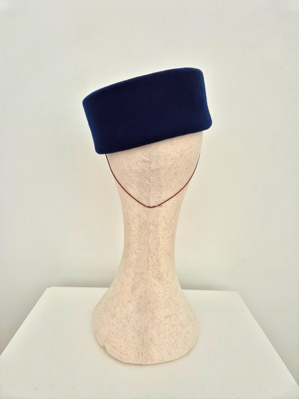 Navy blue felt pillbox headpiece on a mannequin head against a white background back view