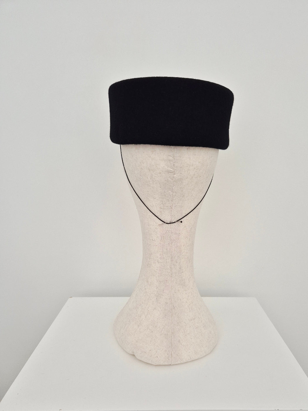 Black felt pillbox headpiece on a maaiguin head back view against a white background