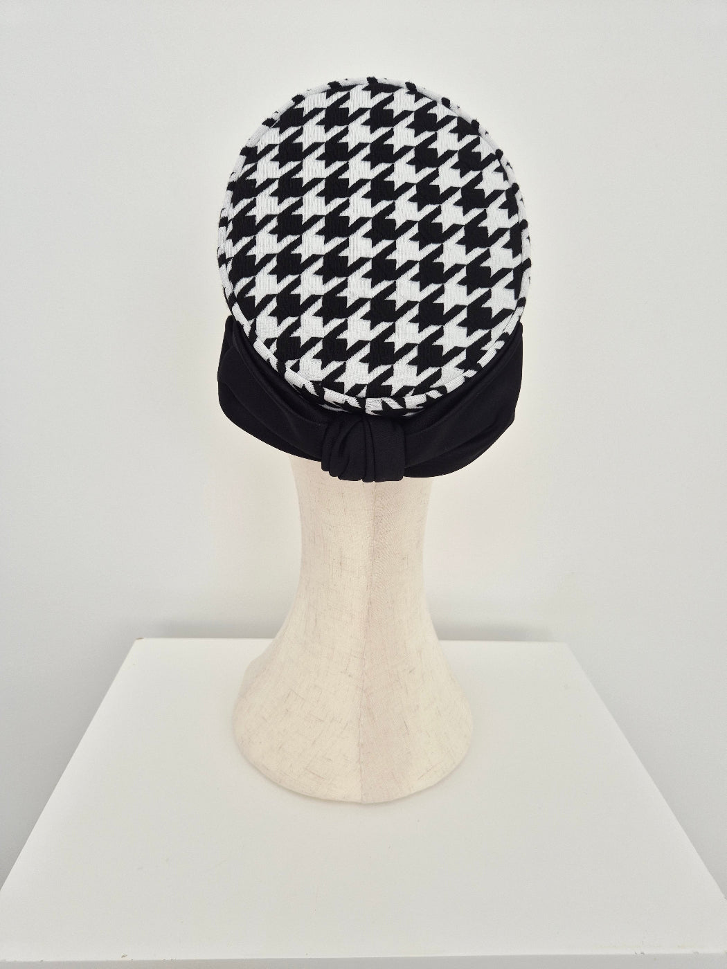 Black and white houndstooth patterned pillbox headpiece on a mannequin head against a white background back view