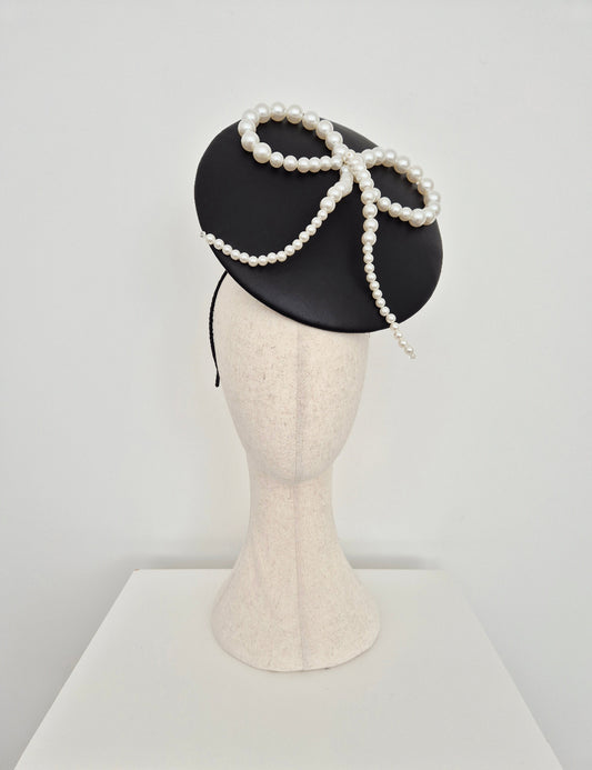 Black leather percher plate hat with pearl bow on a mannequin head against a white background