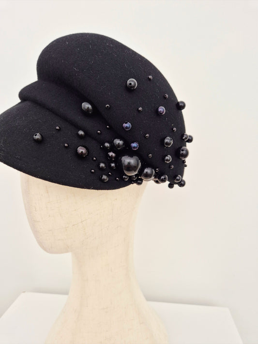 Black hat with bead embellishments on a mannequin head against a white background