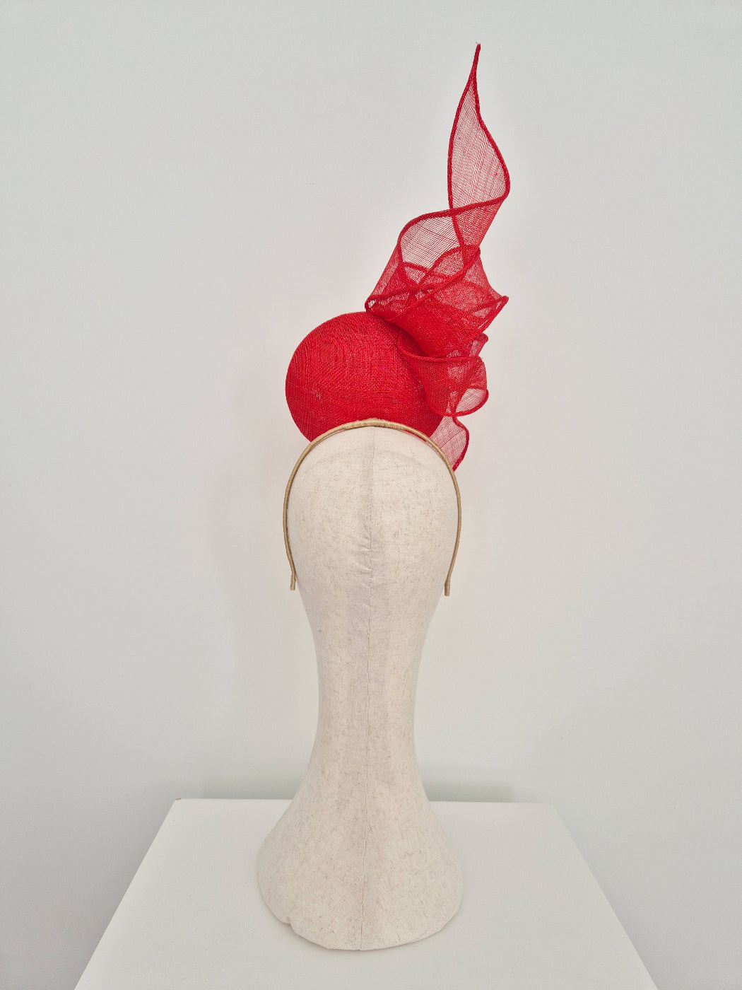 A red fascinator hat with a tall, flowing sheer mesh plume and a structured red base, displayed on a cream-colored fabric mannequin head against a plain white background.back view