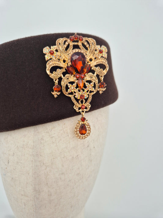 Chocolate brown wool felt pillbox headpiece with brooch on a mannequin head against a white background close up