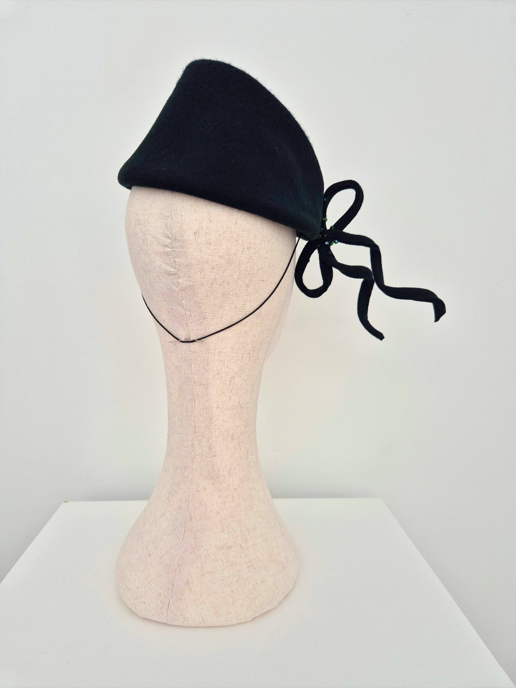 dark forest green topper headpiece with a bow on a mannequin head against a white background back view