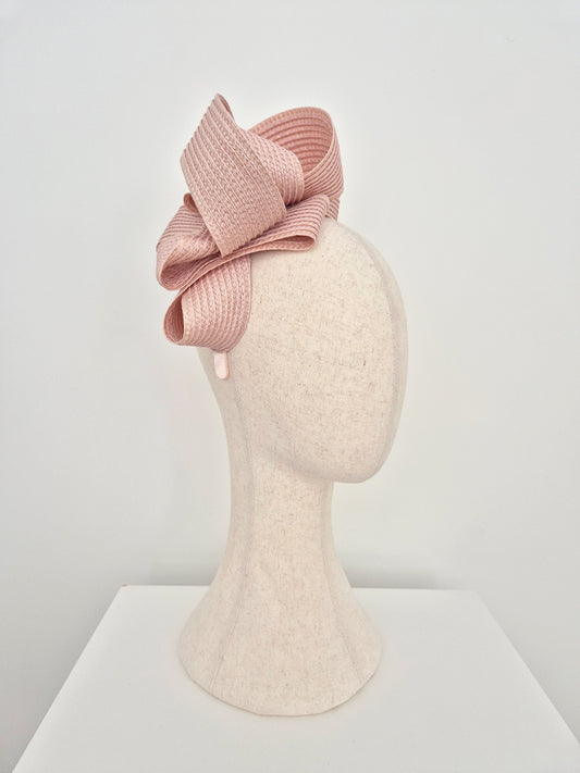 A dusty pink woven ribbon fascinator bow displayed on a textured cream-colored mannequin head, set against a clean white studio background.side view