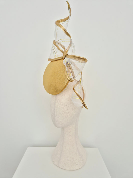 gold button percher millinery with bow and tails on a manniquin head against a white background side view