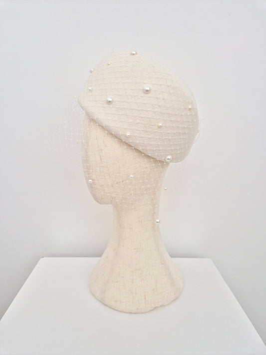 ivory wool felt beret with pearl embellishments on a mannequin head against a white background side view