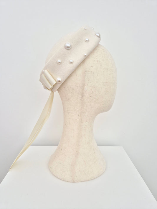 ivory wool felt pillbox headpiece with pearl-like embellishments on a mannequin head against a white background