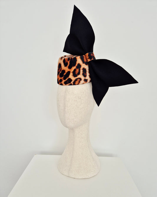 Leopard print headpiece with a black bow on a mannequin head against a white background side view