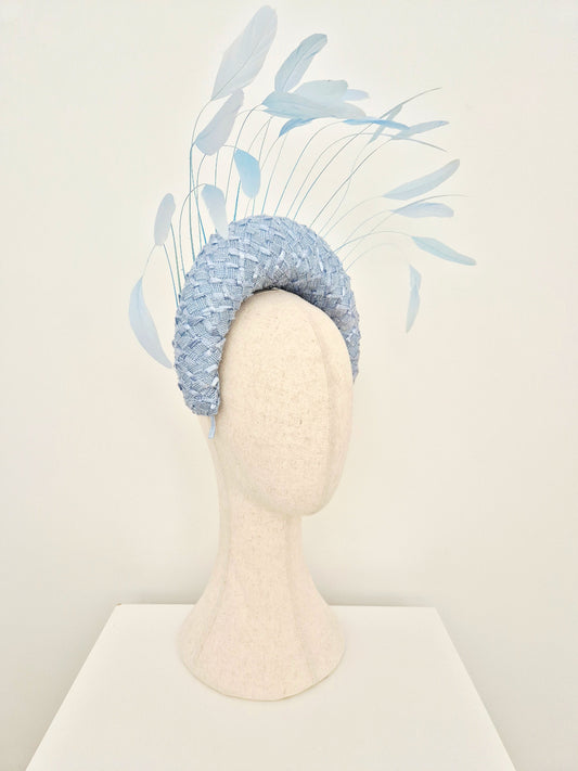 A light blue vintage braid straw fascinator hat with long feather accents, displayed on a cream-colored mannequin head against a plain off-white background.side view