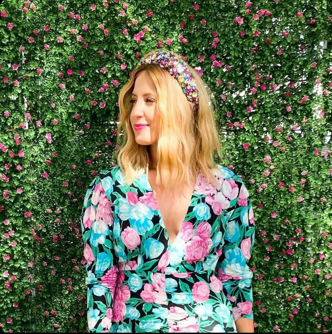 Woman wearing a floral dress and headband in front of a green wall with pink flowers