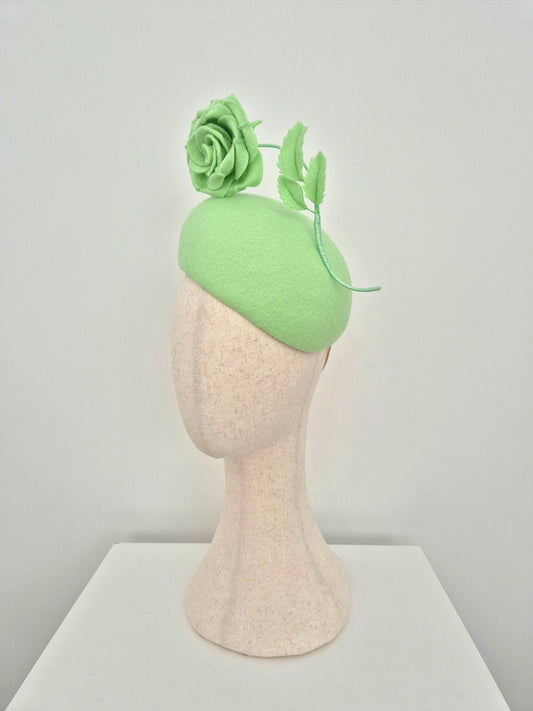 Green headpiece with floral details on a mannequin head against a plain background side view