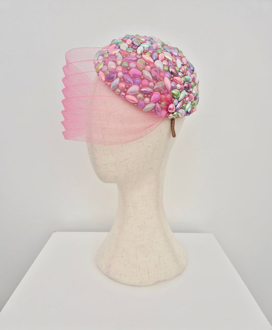 Mannequin head wearing a colorful beaded headpiece with face veil on a white background side view