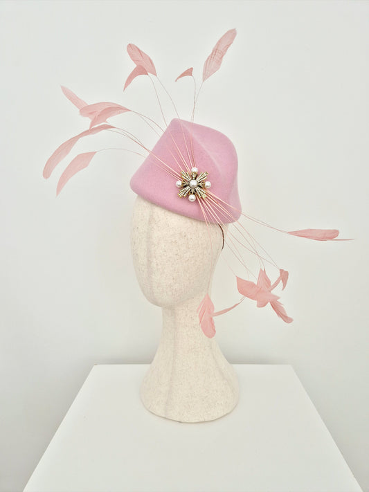 Pink felt headpiece with feathers on a mannequin head against a white background side view