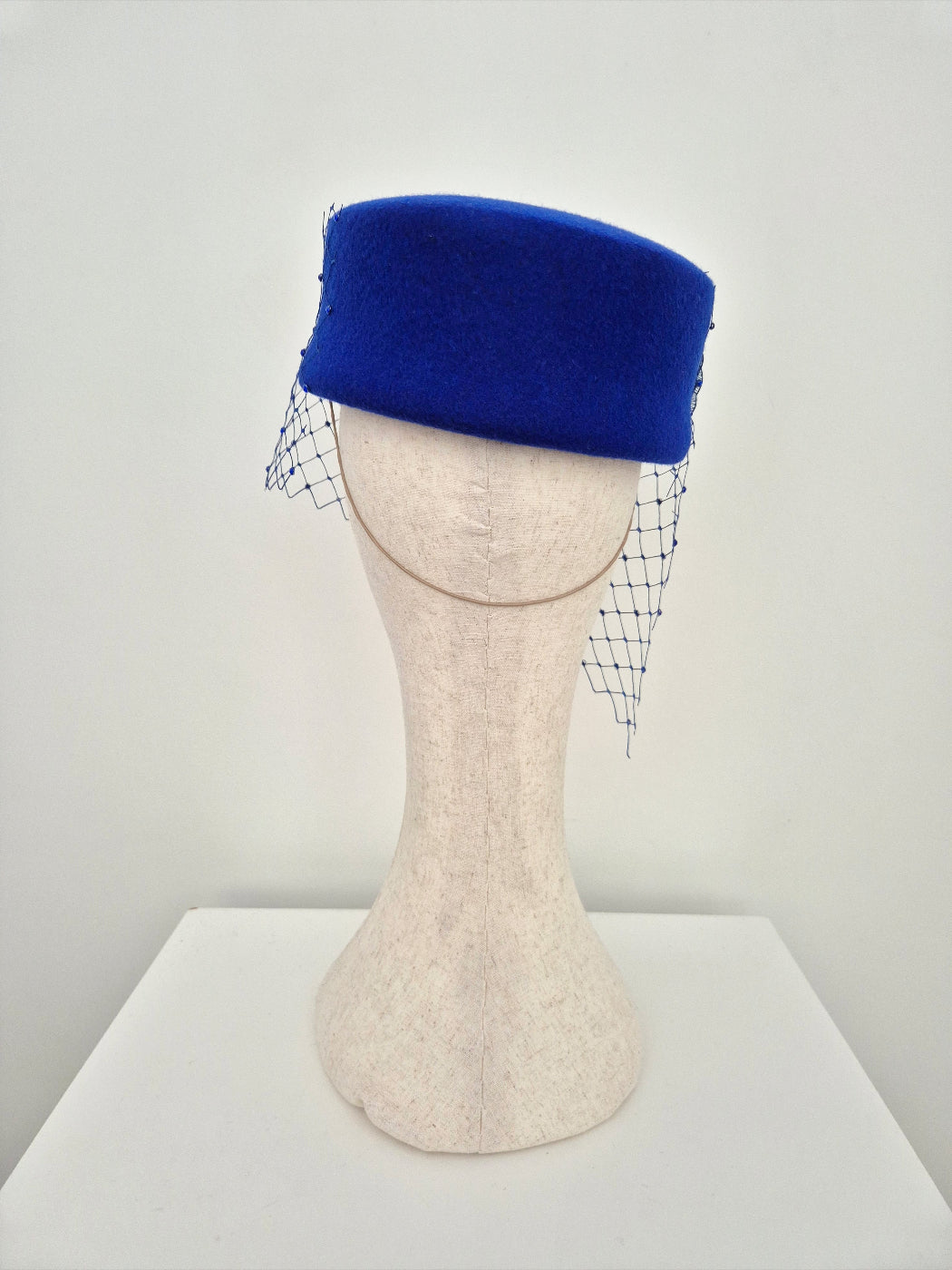 Blue felt hat with a net veil on a mannequin head against a plain background back view
