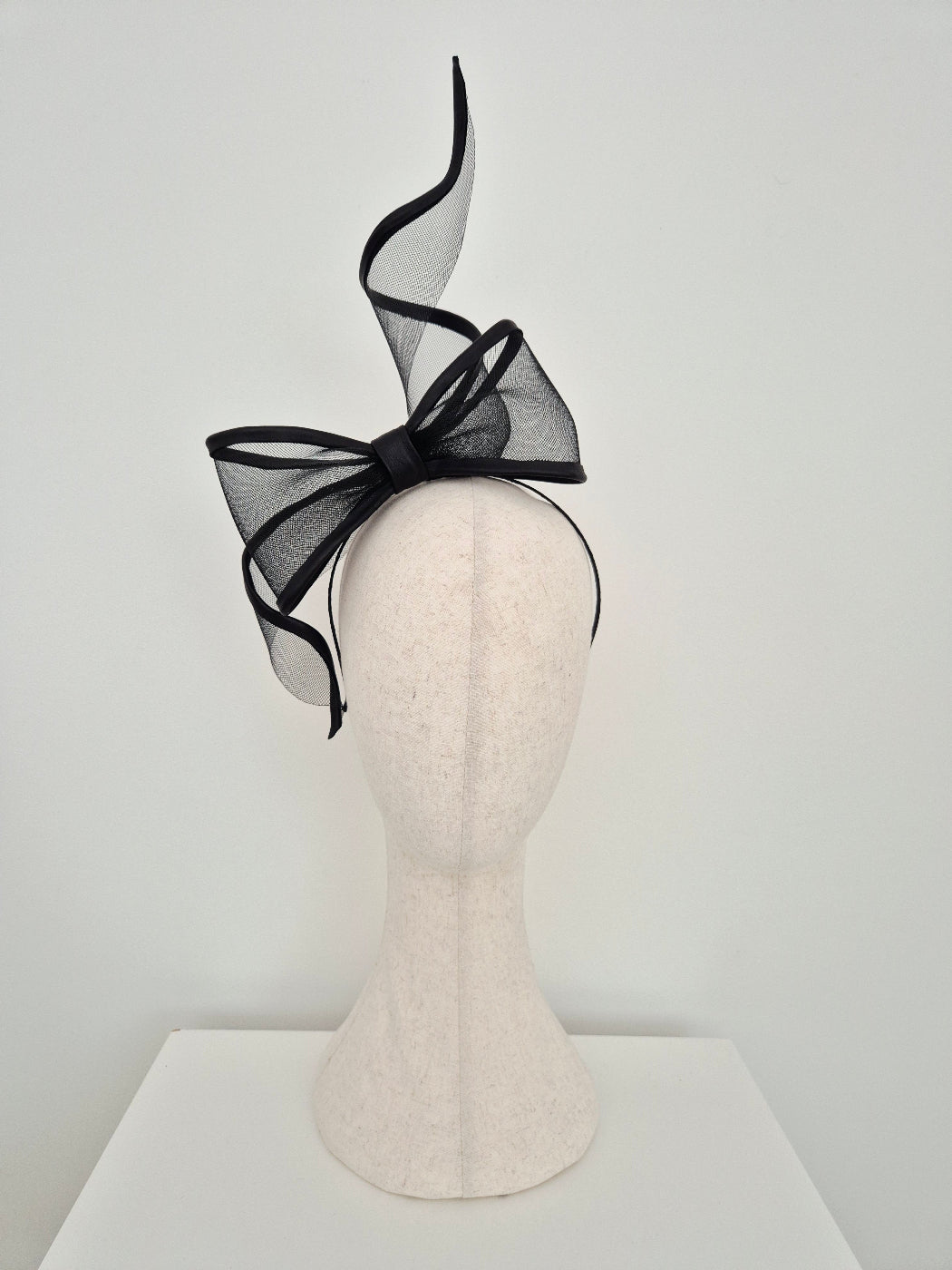 Black decorative bow on a mannequin head against a white background