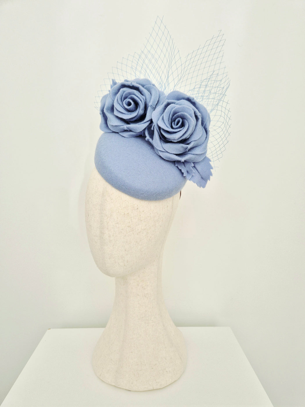 Dusty blue fascinator with flowers on a mannequin head against a white background side view