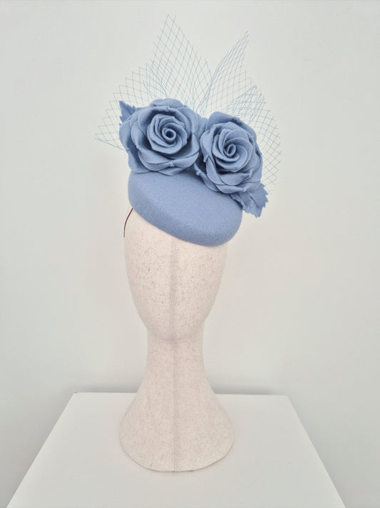 Light blue fascinator with floral decorations on a mannequin head against a white background