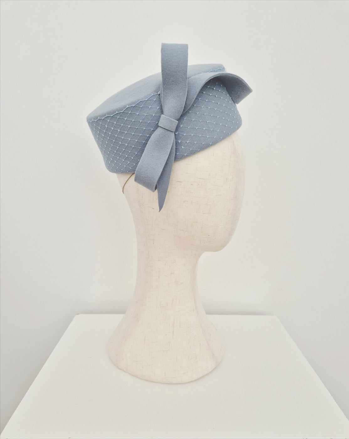 Dusty blue pillbox headpiece on a mannequin head against a white background