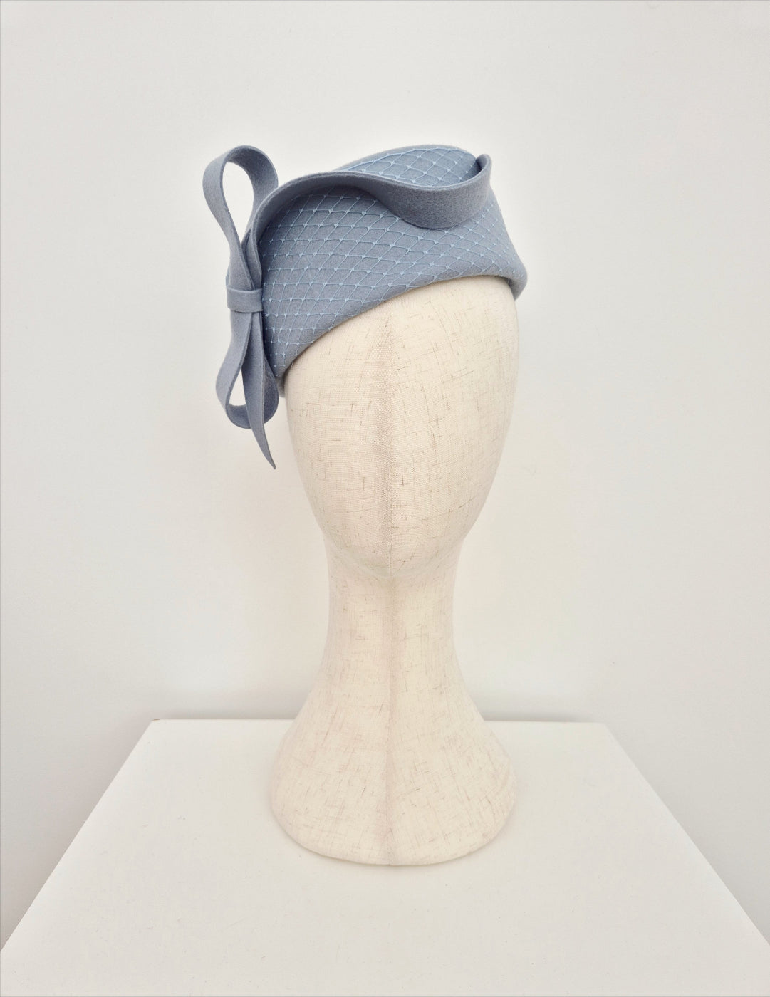 Dusty blue felt pillbox on a mannequin head against a white background