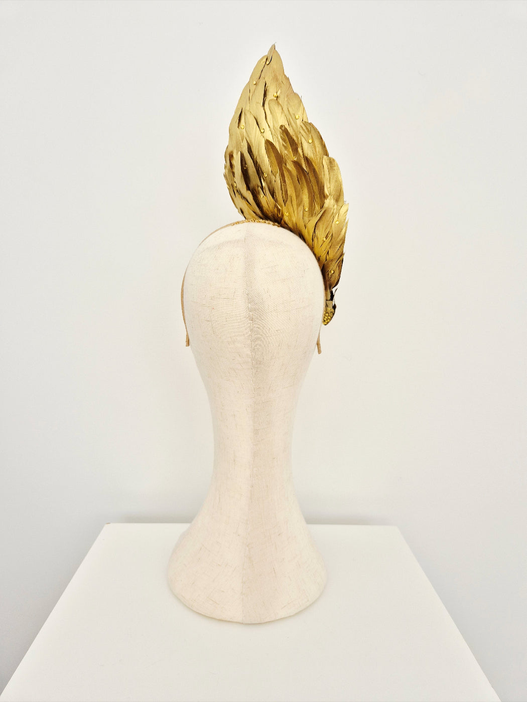 Mannequin head with a gold feather headpiece back view on a white background