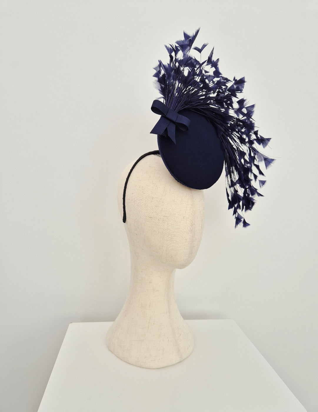 Navy blue fascinator with feathers on a mannequin head against a white background side view