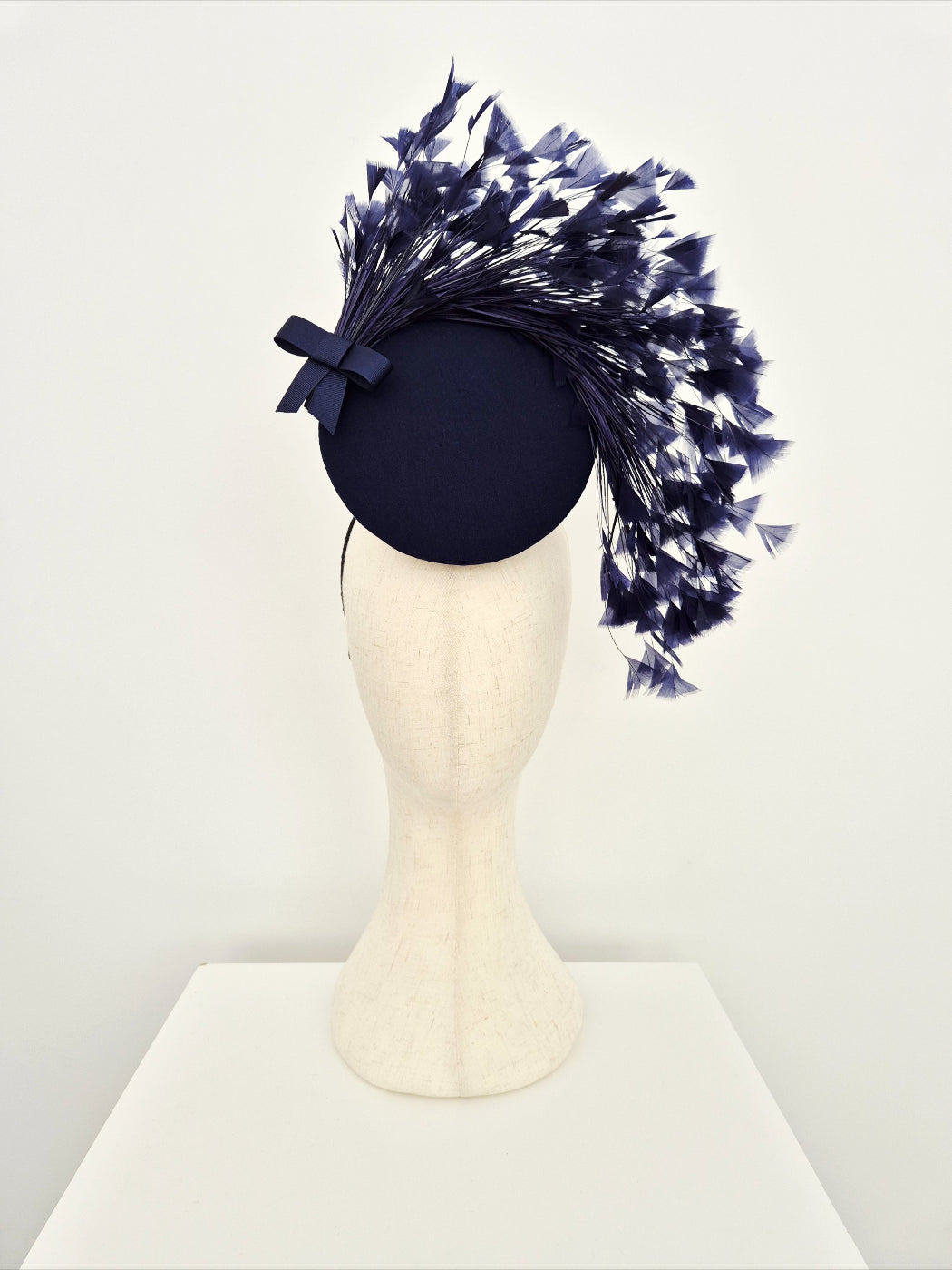 Navy blue fascinator with feather on a mannequin head against a white background