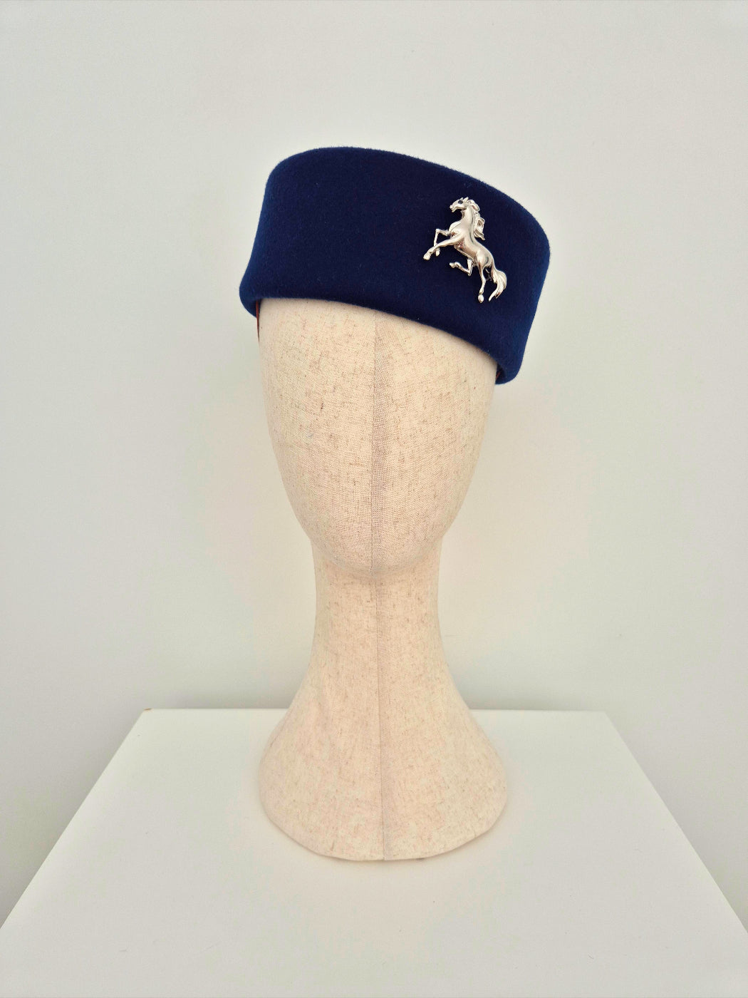 Navy blue pillbox hat with a horse emblem on a mannequin head against a white background