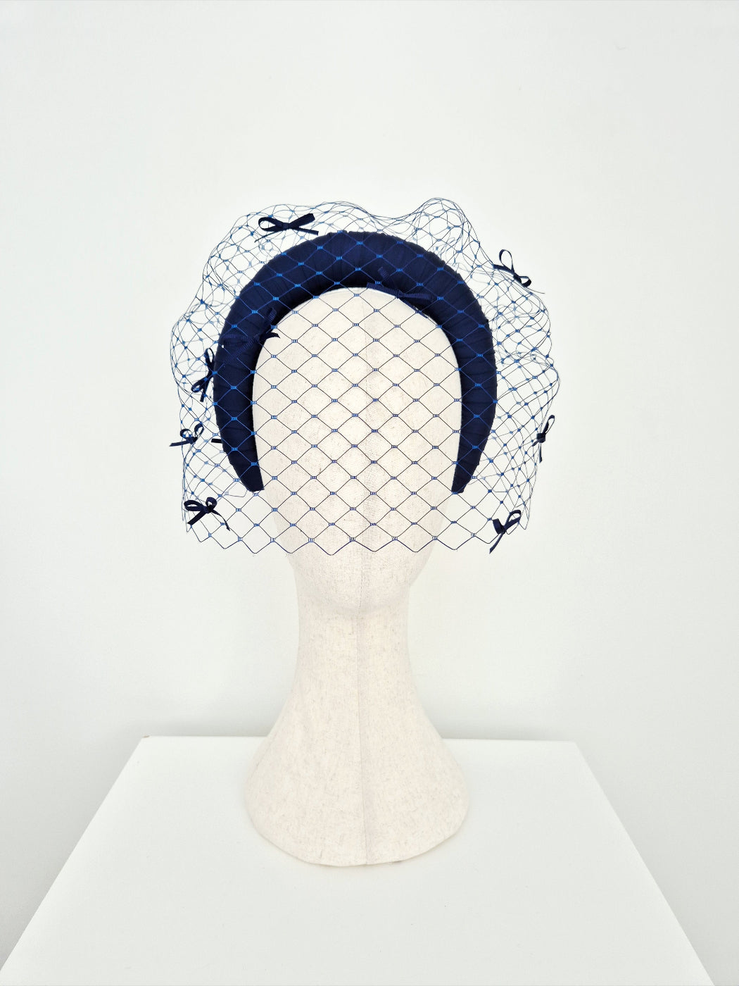 Navy blue headband with a veil and bows on a mannequin head against a white background