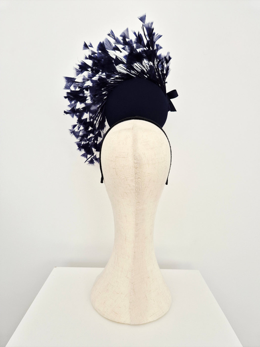 Navy blue percher headpiece with feathers on a mannequin head against a white background back view