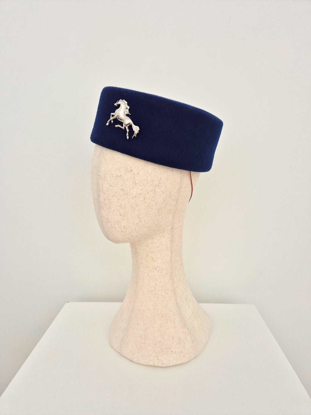 Navy blue hat with a horse emblem on a mannequin head against a white background side view
