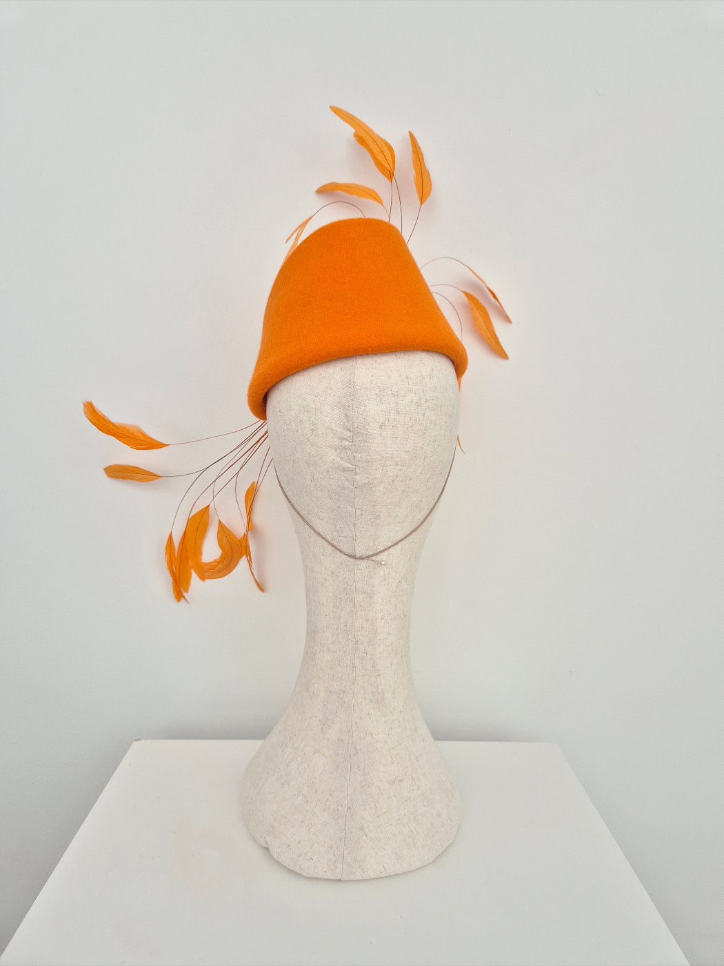 Orange hat with feather accents on a mannequin head against a white background back view