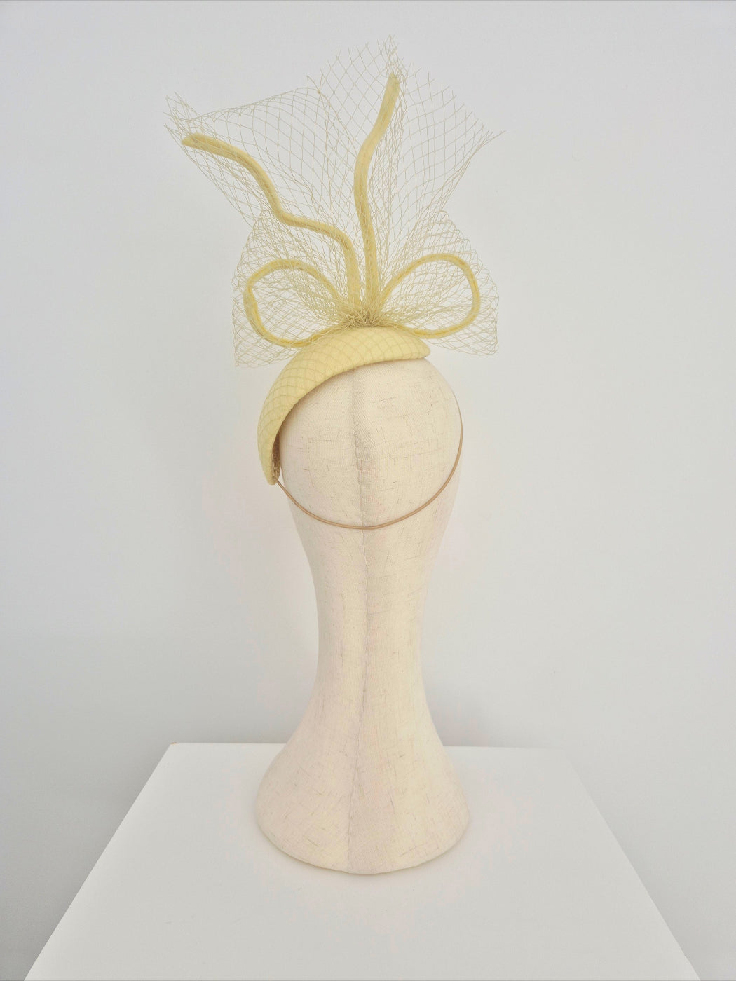 Pale yellow headpiece with bow and veiling on a mannequin head against a white background back view