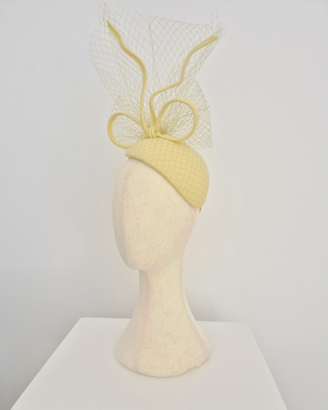 Pale Yellow headpiece with bow and veiling on a mannequin head against a white background side view