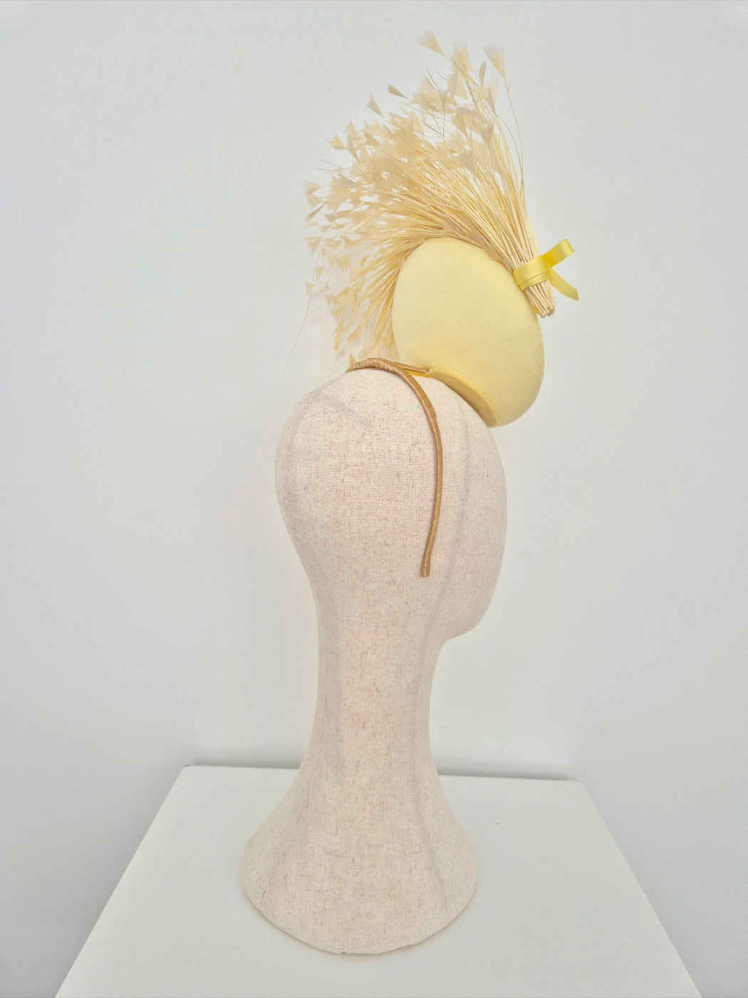 Yellow fascinator on a mannequin head against a white background side back view
