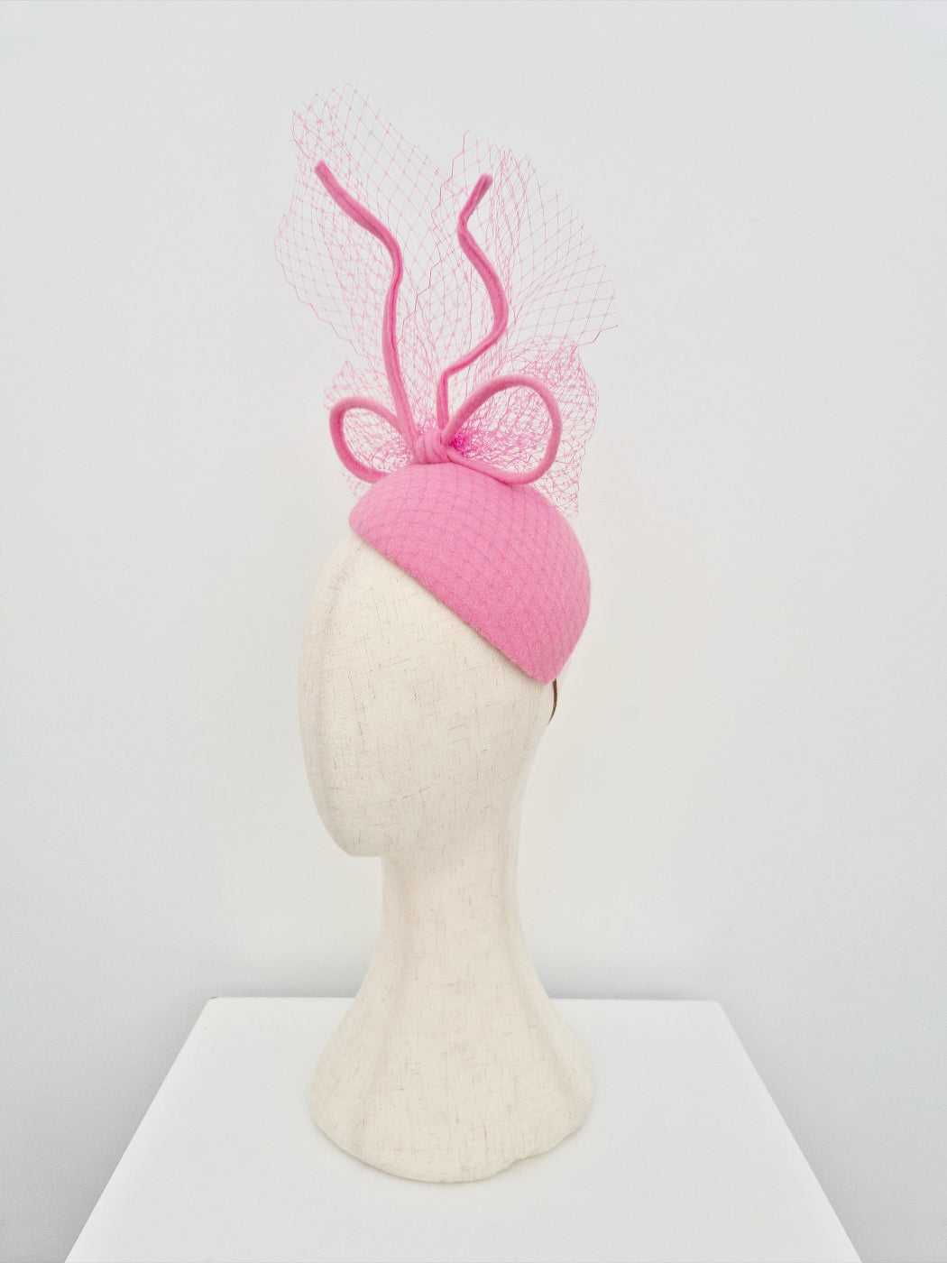Pink headpiece with bow on a mannequin head against a white background side view