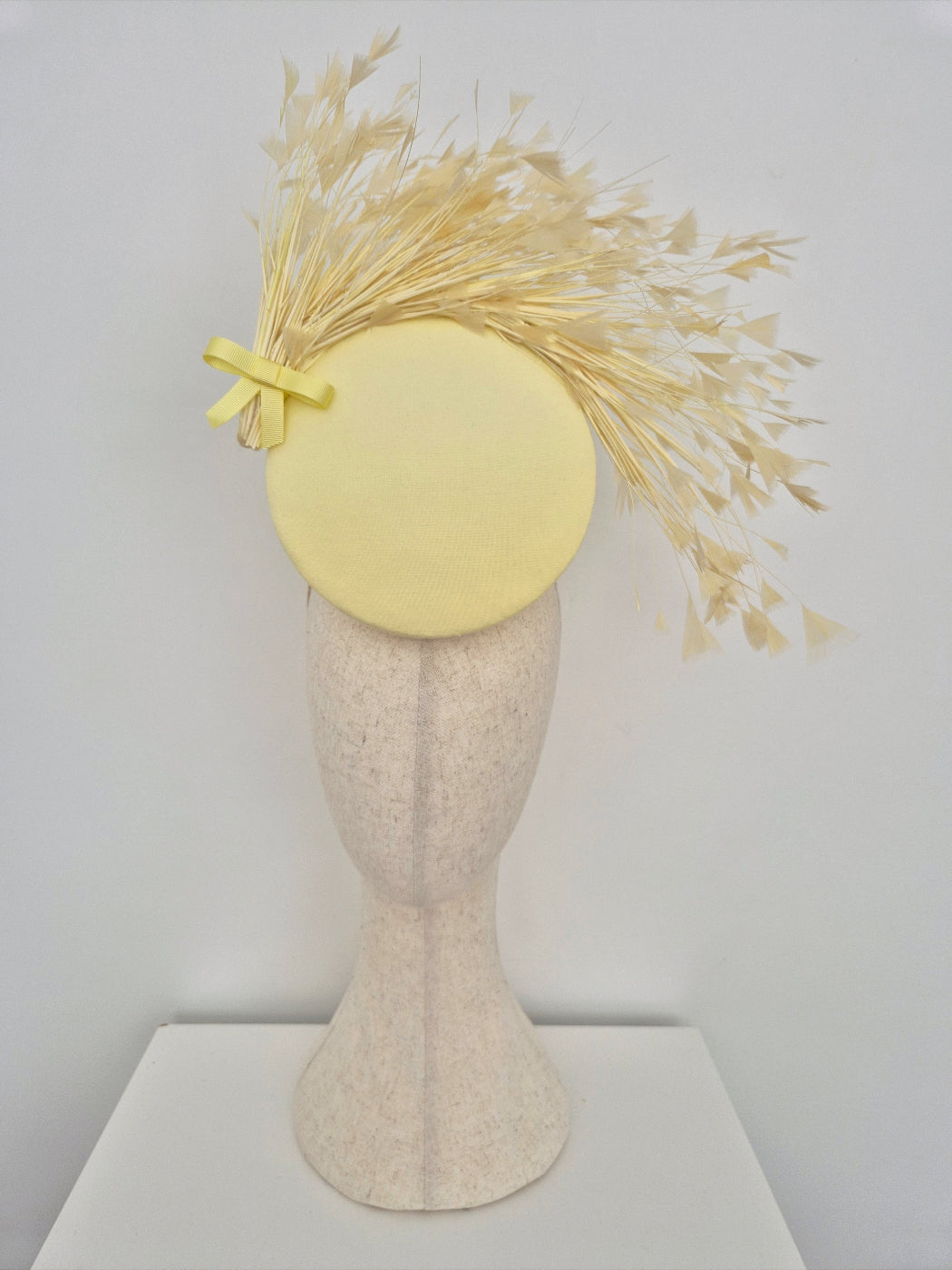 Yellow fascinator with feathers on a mannequin head against a white background