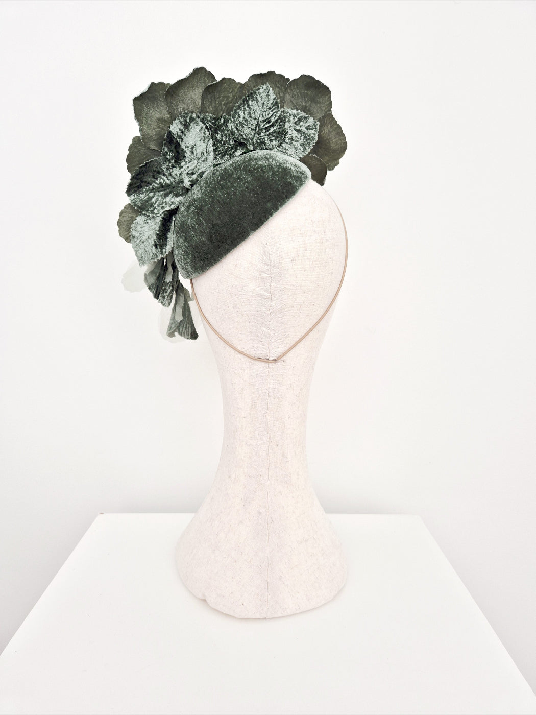 Sage green floral headpiece on a mannequin head against a white background back view