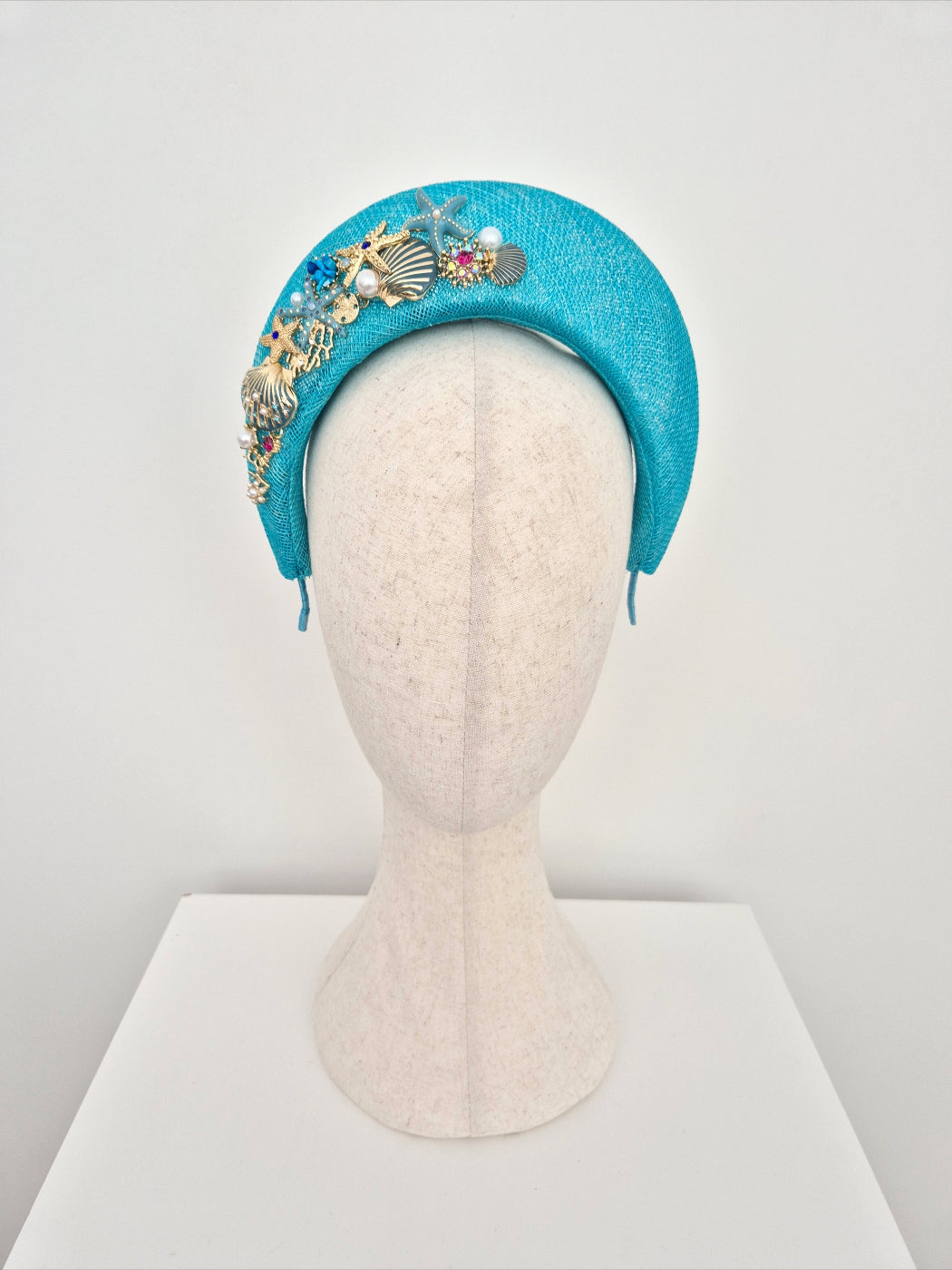 Turquoise headband with decorative elements on a mannequin head against a white background