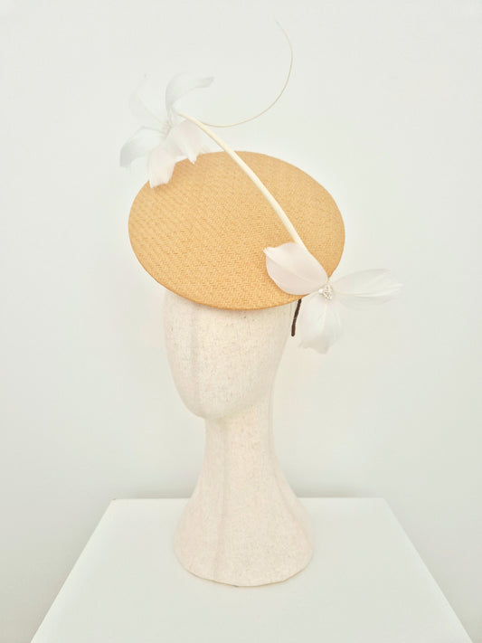 A light beige woven straw percher fascinator headpiece with white feather flowers and a curved feather accent, displayed on a textured cream mannequin head against a white background. side view