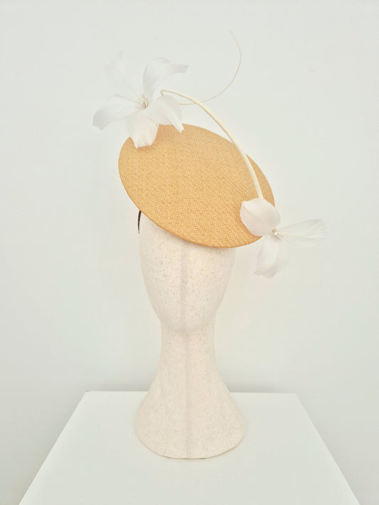 A light beige percher fascinator with white feather flowers and a long feather accent, displayed on a textured cream mannequin head against a white background.