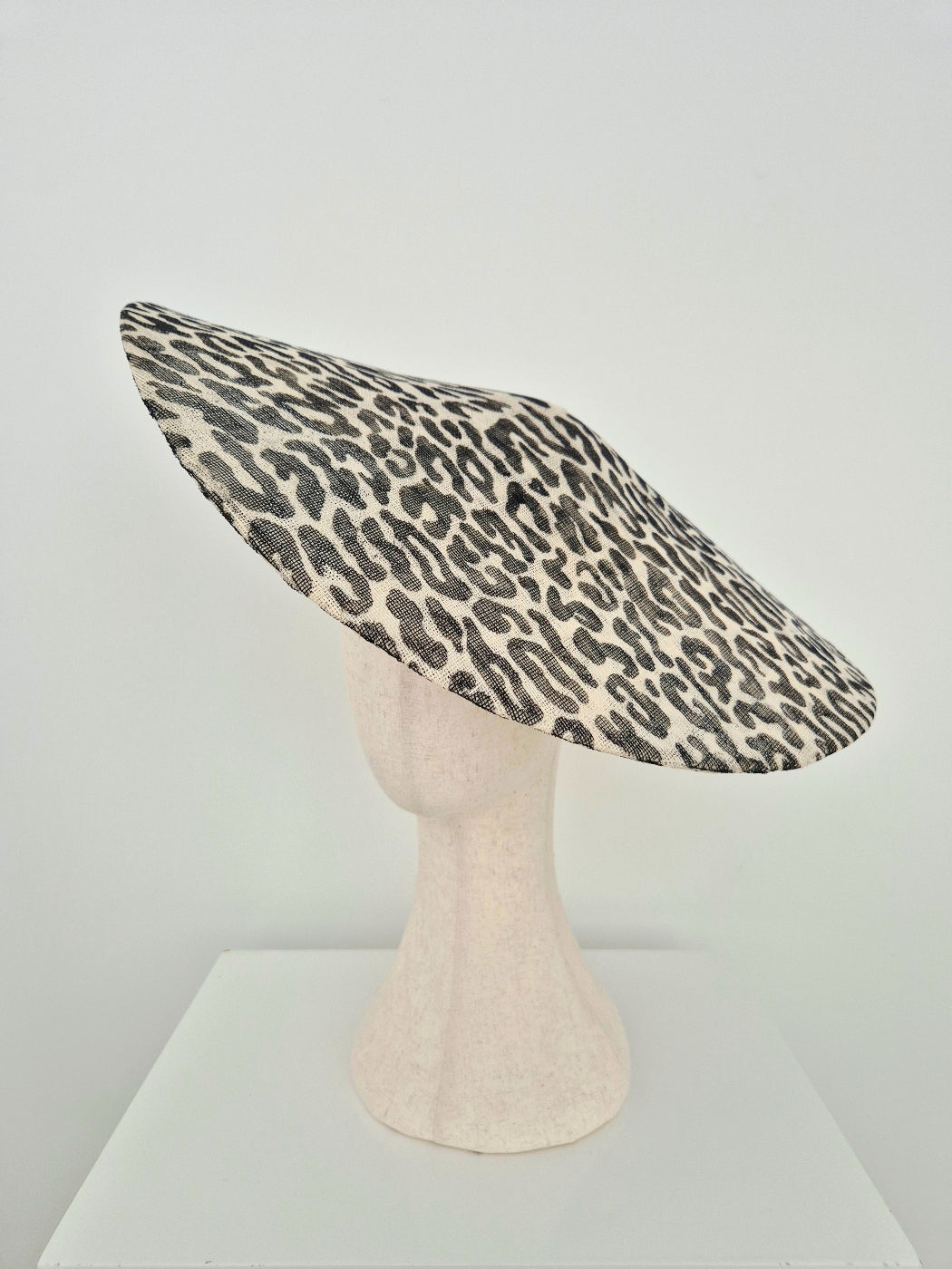 A leopard print straw hat displayed on a textured mannequin head stand against a plain white studio background. side veiw