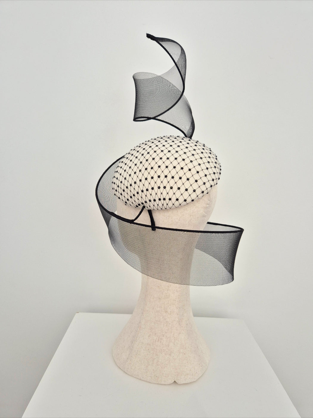 Black and ivory decorative headpiece on a mannequin head against a plain background side back view