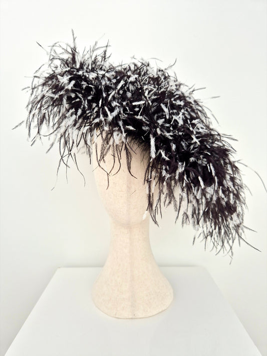 A dramatic black feather fascinator or hairpiece with white feather accents, displayed on a beige mannequin head against a plain white background.