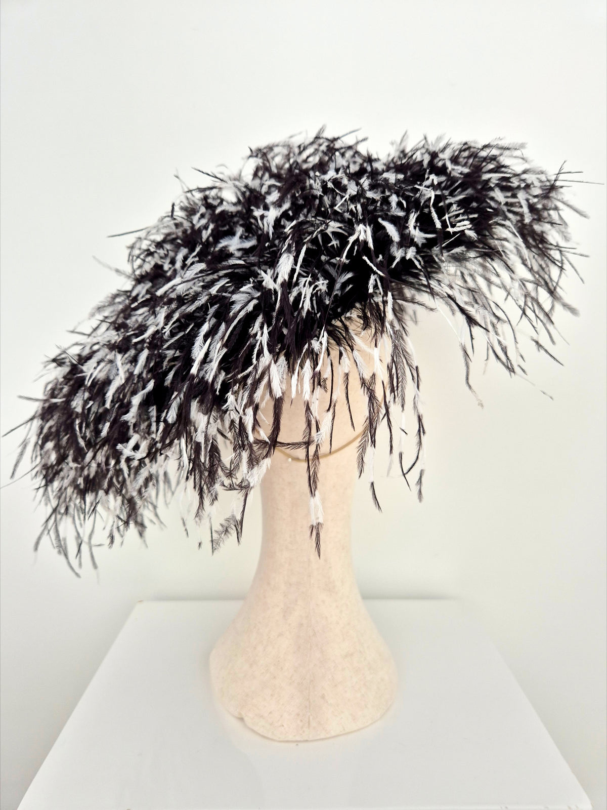 A voluminous black feather boa with white feather accents, displayed on a beige mannequin head against a plain white background.back view