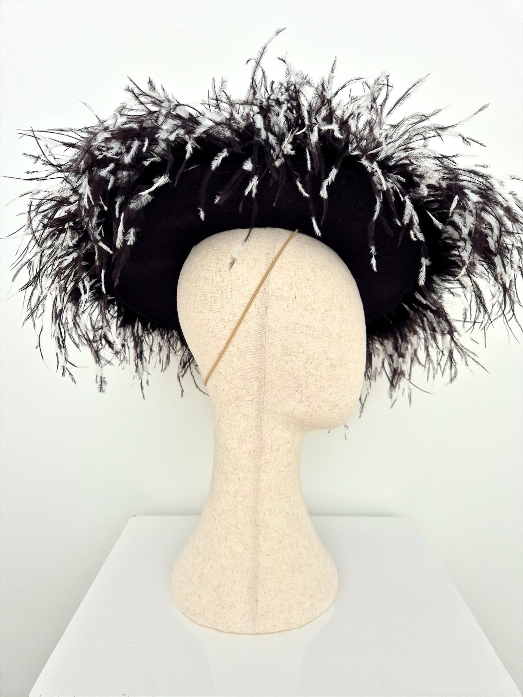 A black feather fascinator hat displayed on a beige fabric mannequin head against a plain white background.underside