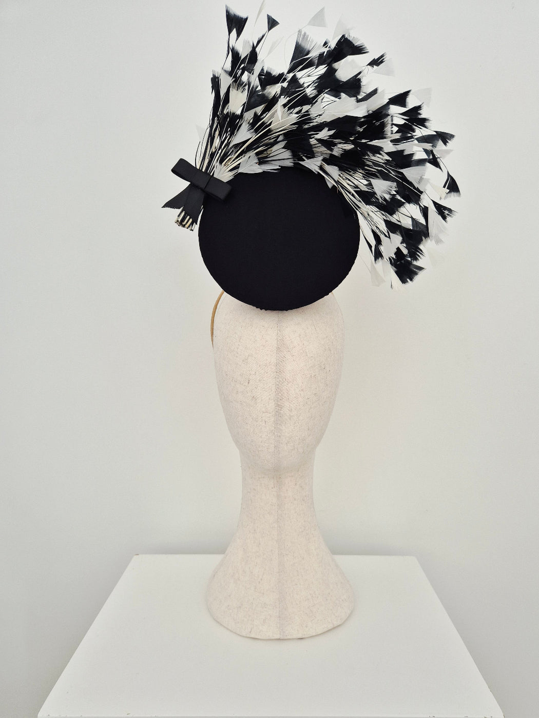 black and white feather percher headpiece on a manniquin head against a white background