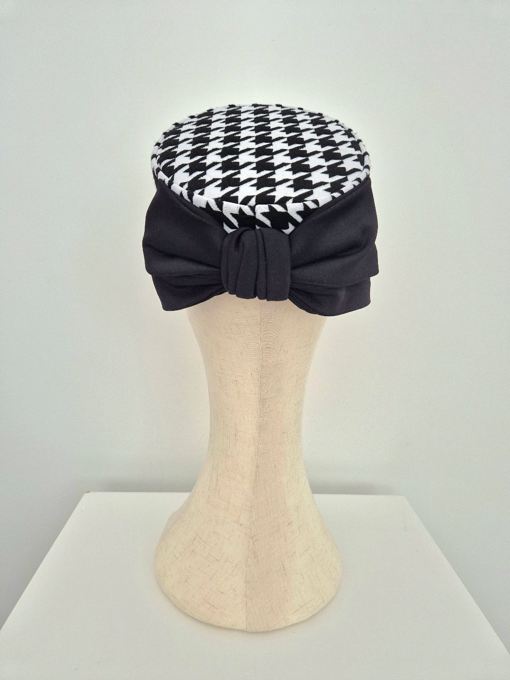Black and white houndstooth patterned headpiece pillbox on a mannequin head against a white background