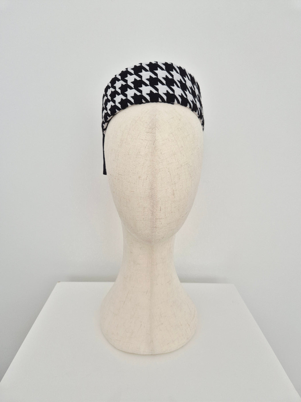 Black and white houndstooth pillbox headpiece on a mannequin head against a light gray background